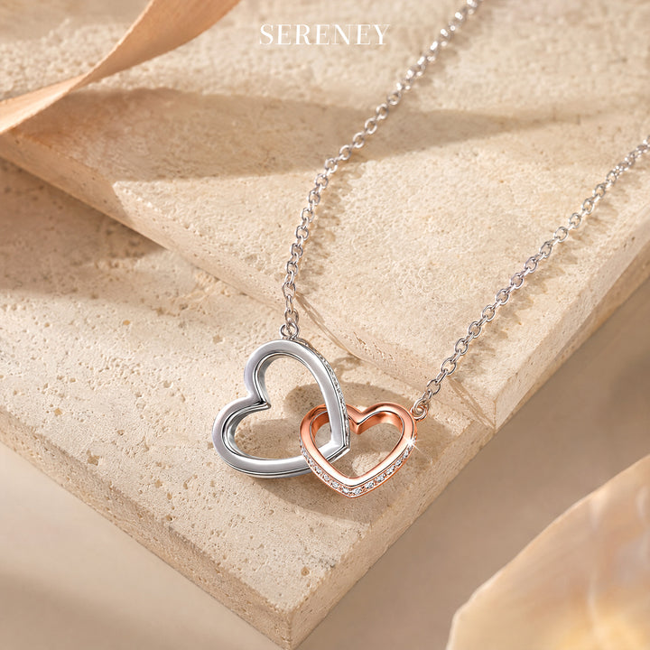 Close-up of interlocking heart necklace on a textured surface