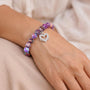Purple bead bracelet with silver heart charm worn on a hand