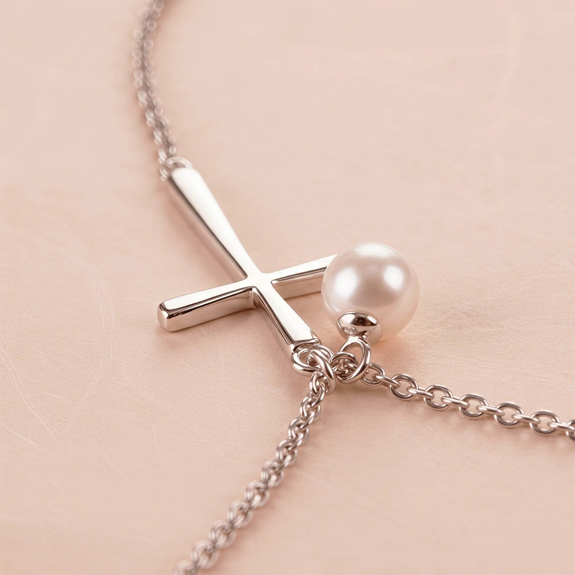 Close-up of silver cross necklace with pearl charm