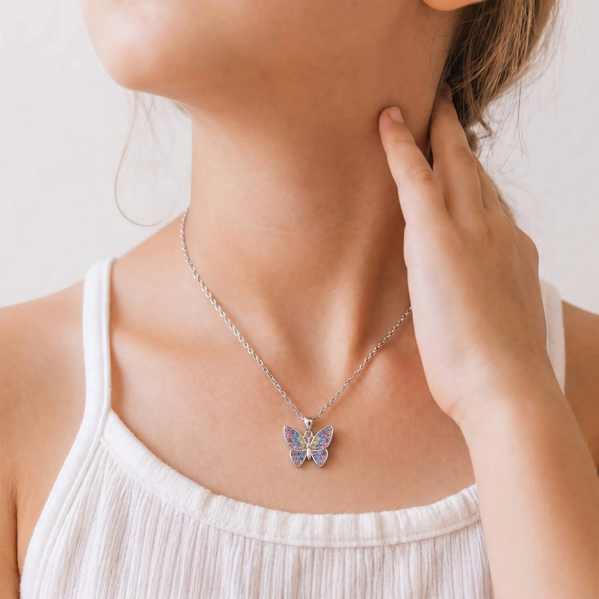Small colorful butterfly pendant necklace on silver-tone chain, worn with white tank top