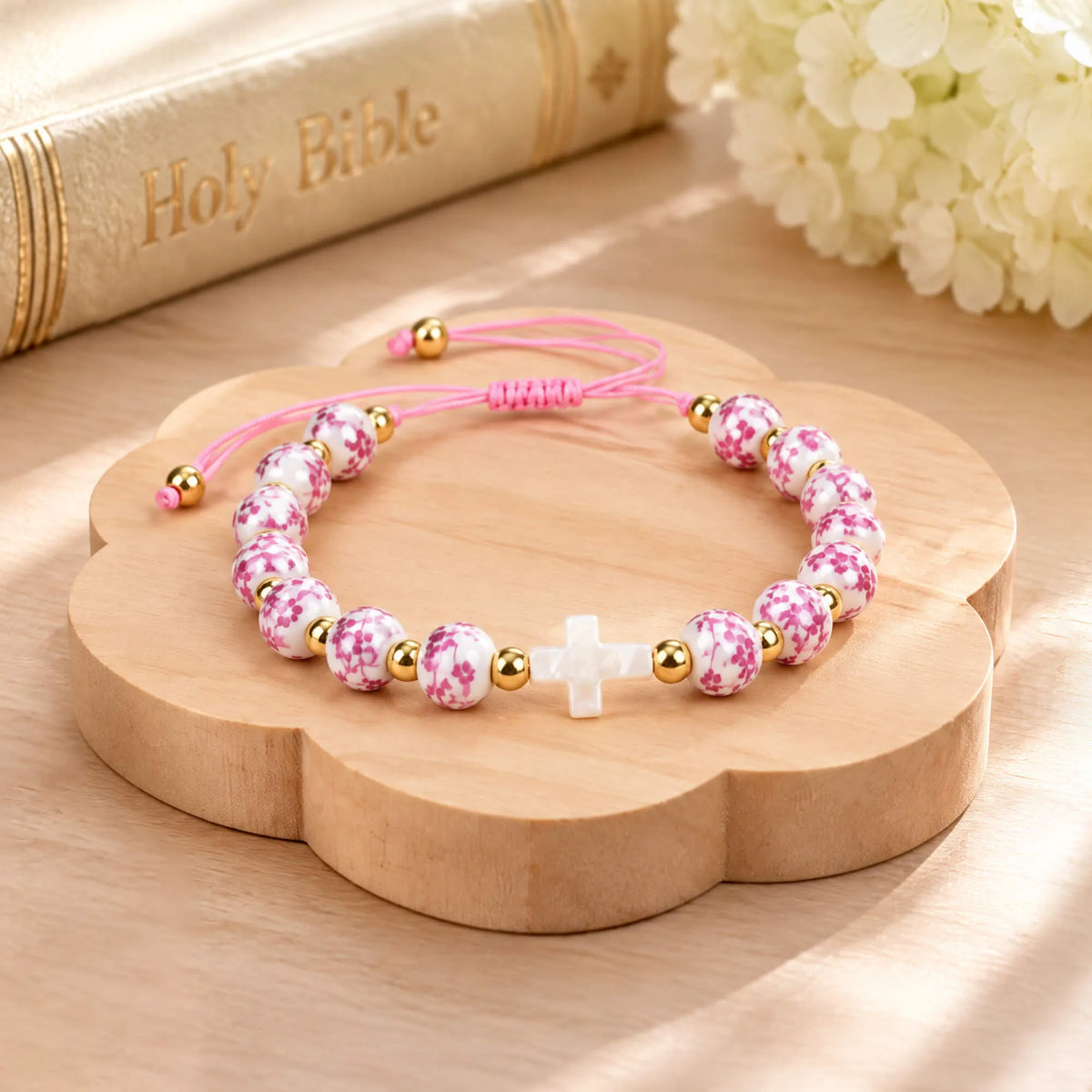 Pink beaded cross bracelet on a round wooden display with gold spacer beads