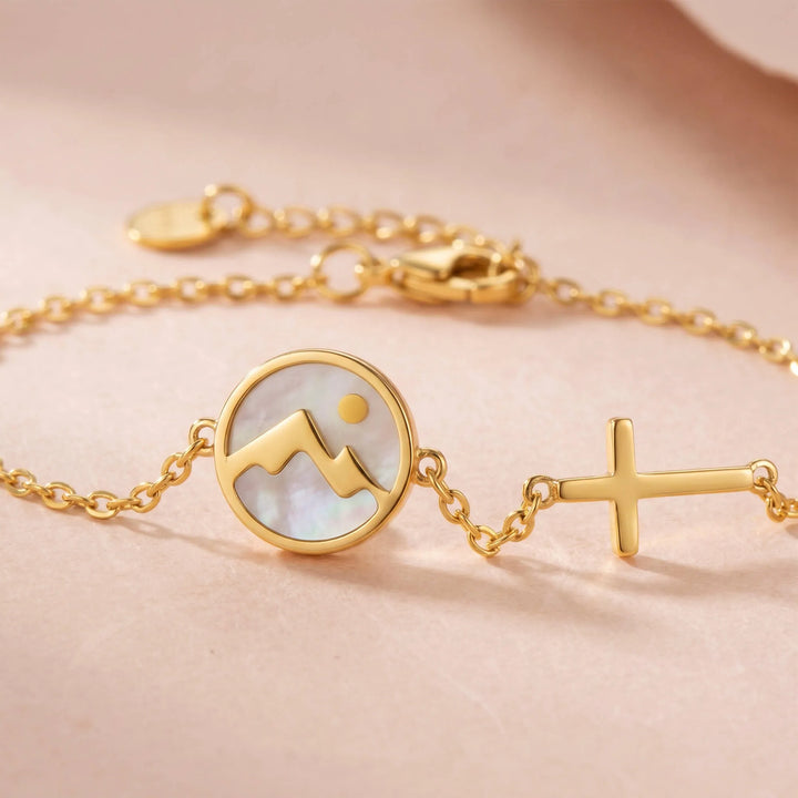 Close-up of gold bracelet with mountain charm and cross on skin