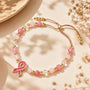 Pink and gold beaded bracelet with ribbon charm and adjustable brown cord