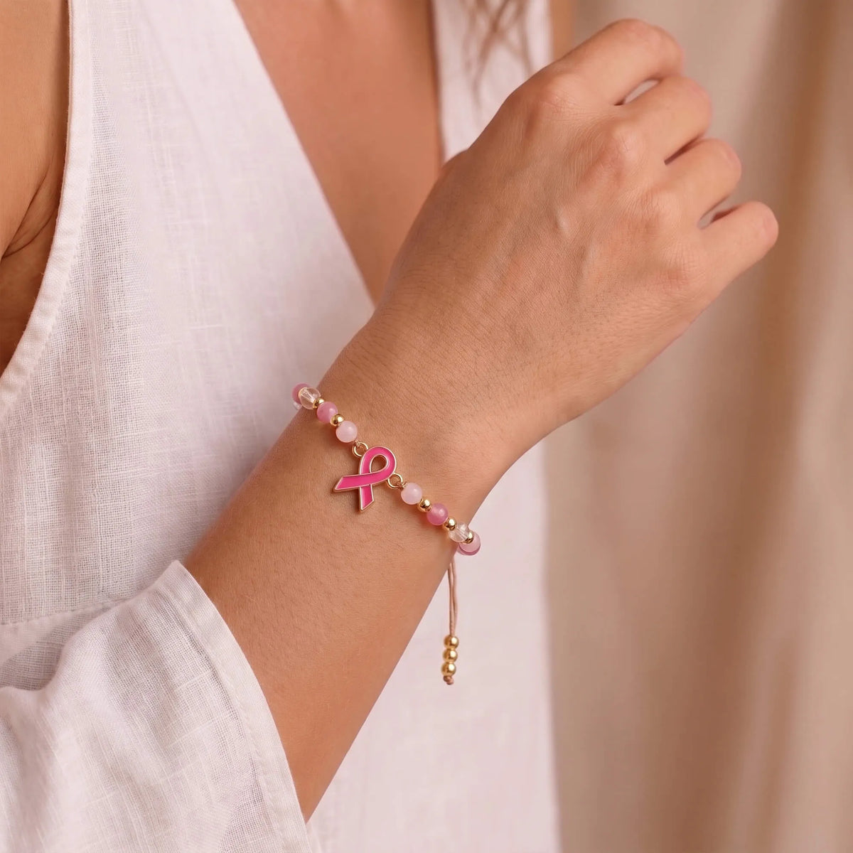 Pink beaded ribbon charm bracelet worn on wrist with brown cord ties
