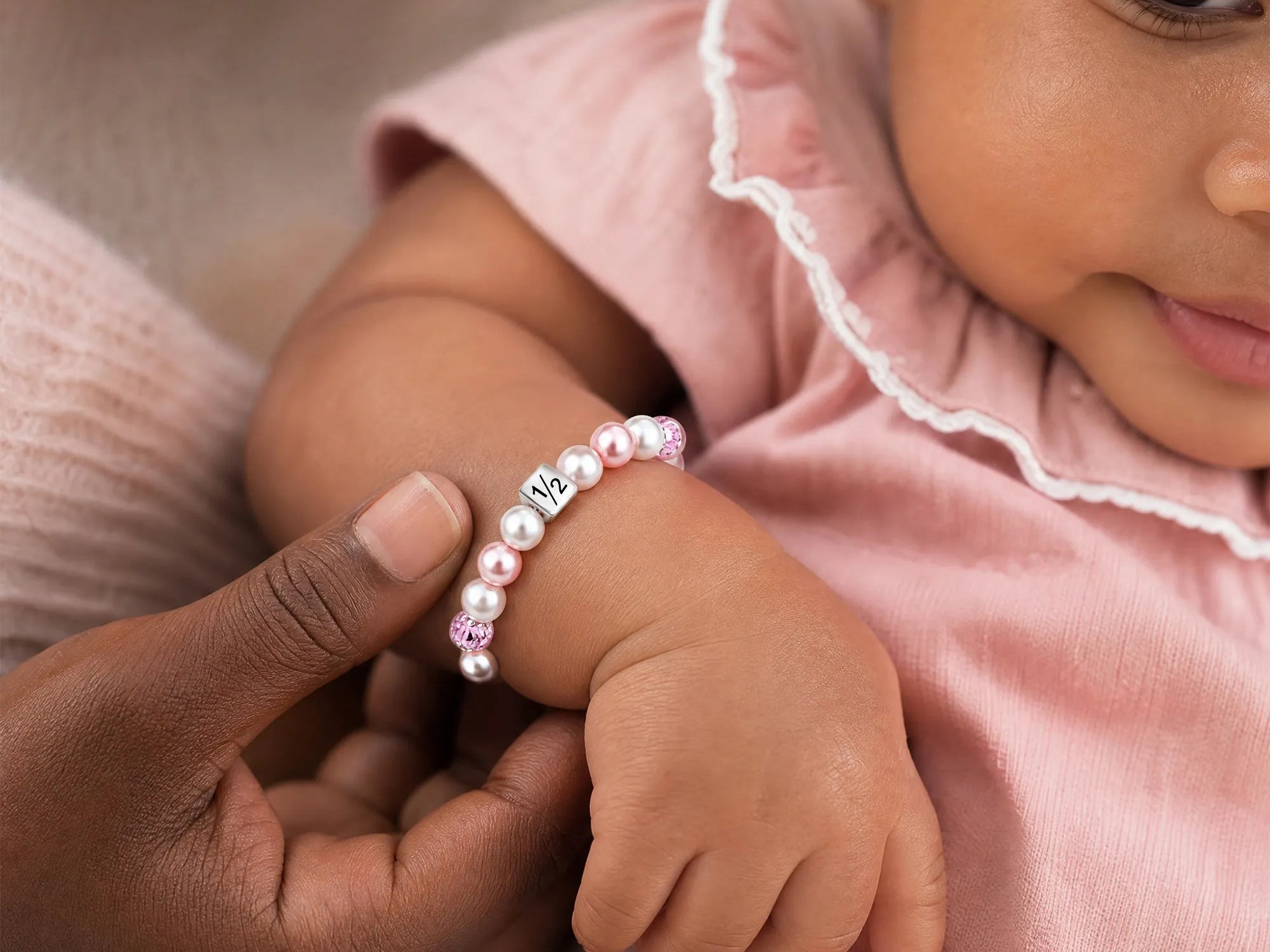Baby wearing pink pearl bracelet with number 1/2