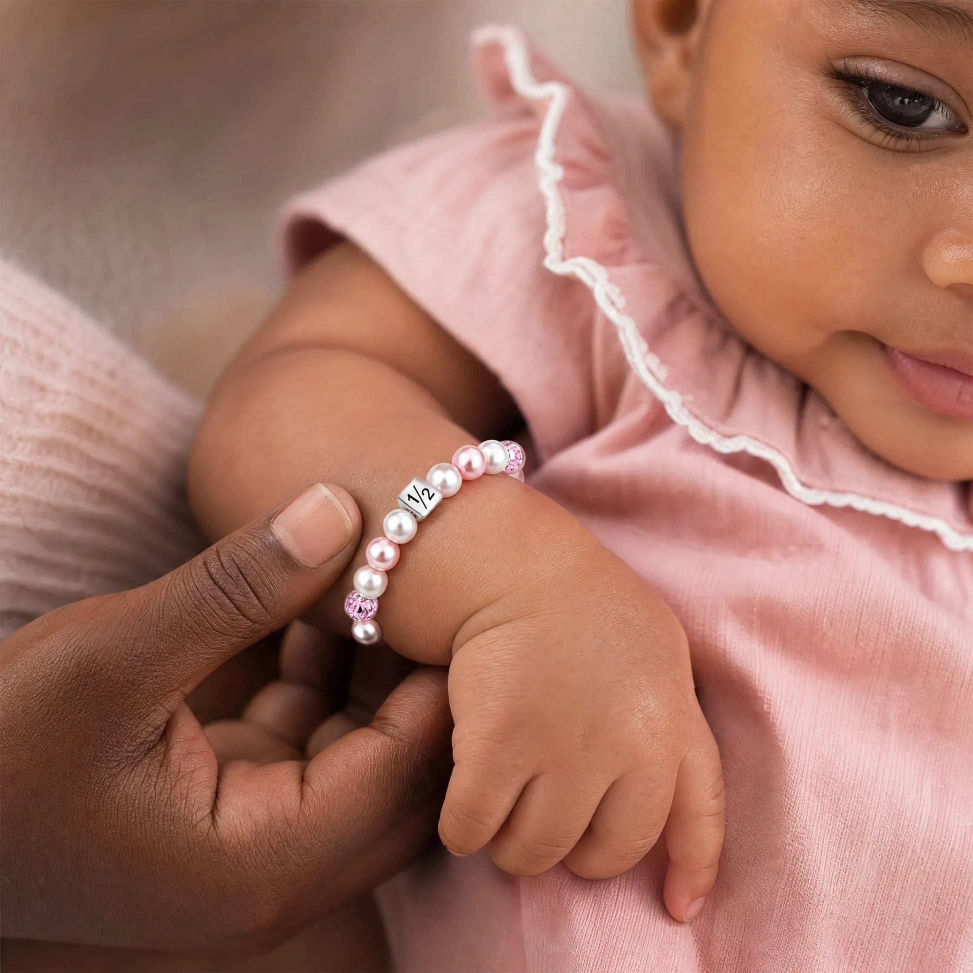 Baby wearing pink pearl bracelet with number 1/2