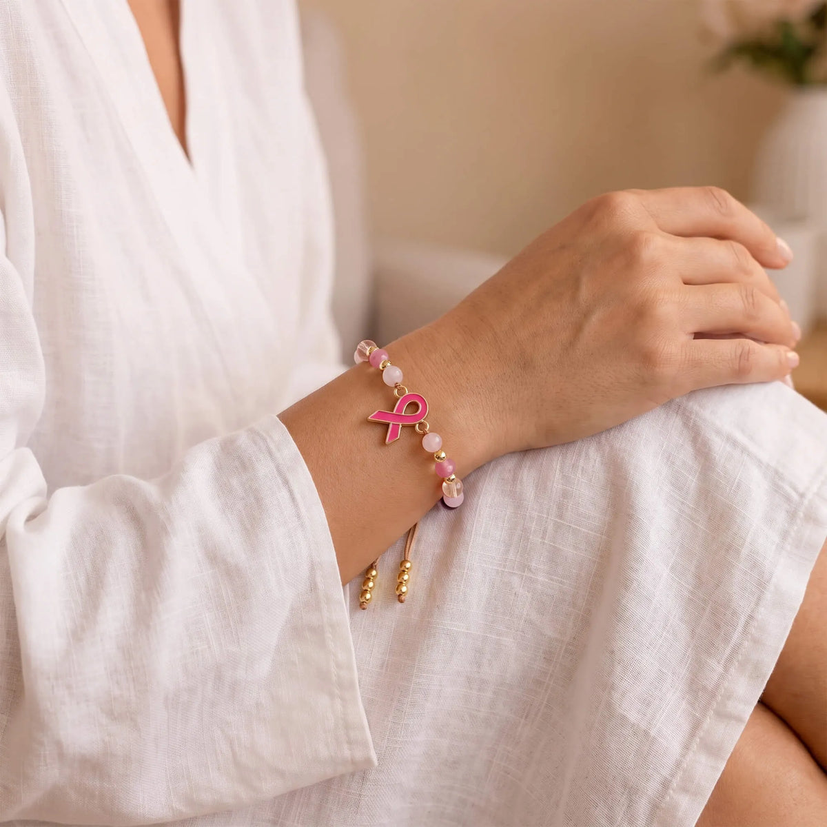 Pink ribbon charm bracelet on wrist with gold bead accents and brown cord