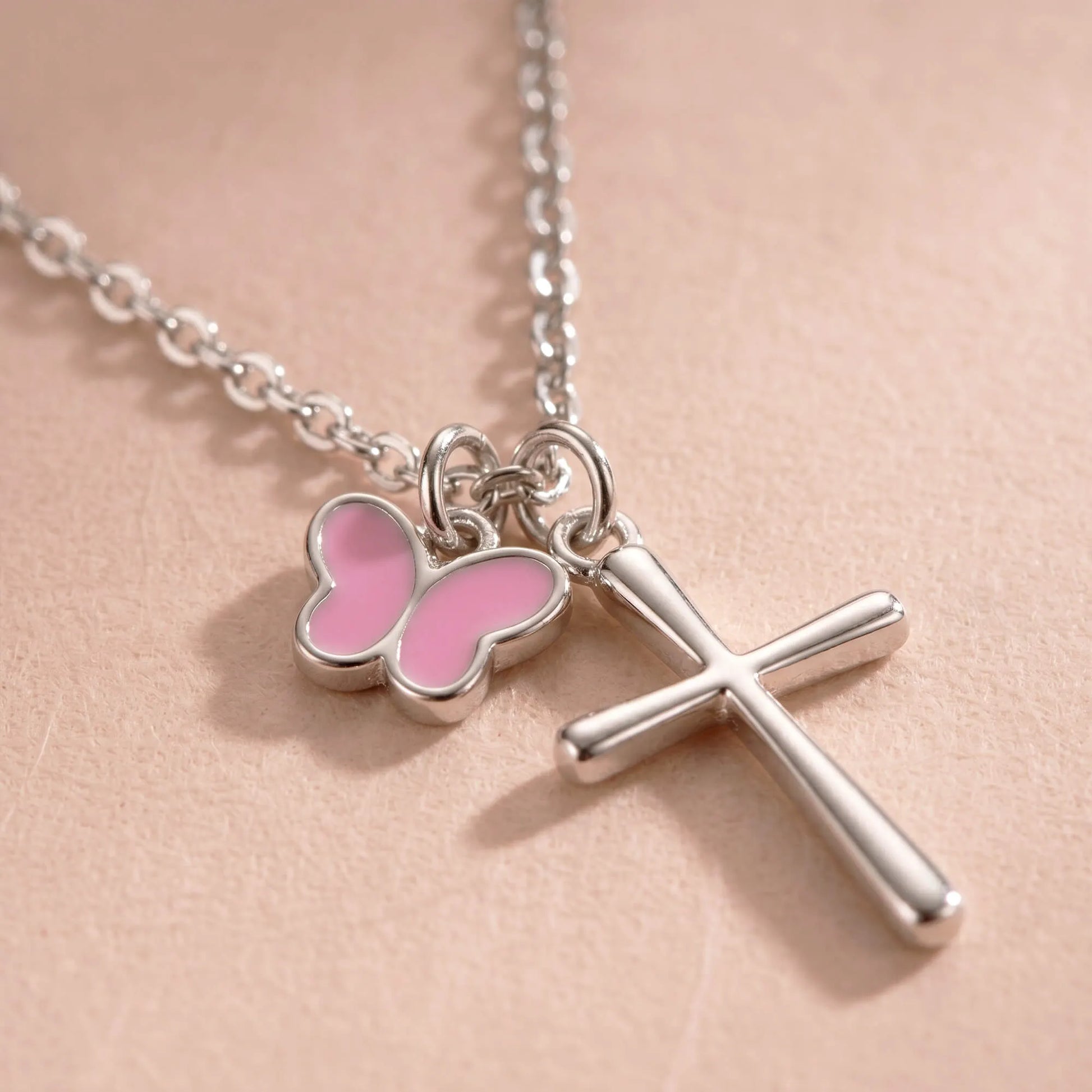 Close-up of silver cross necklace with pink butterfly charm
