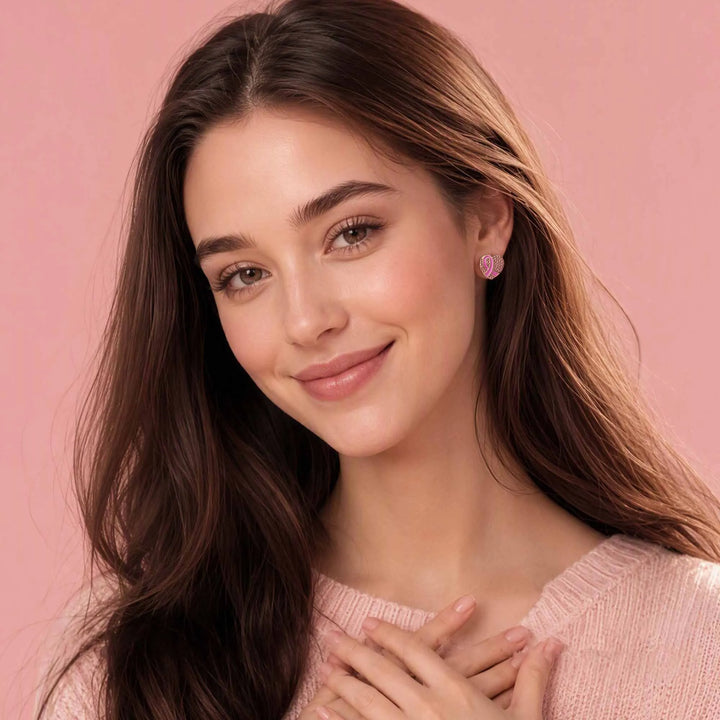 Pink ribbon heart earrings worn by a woman, small stud style
