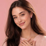 Pink ribbon heart earrings worn by a woman, small stud style