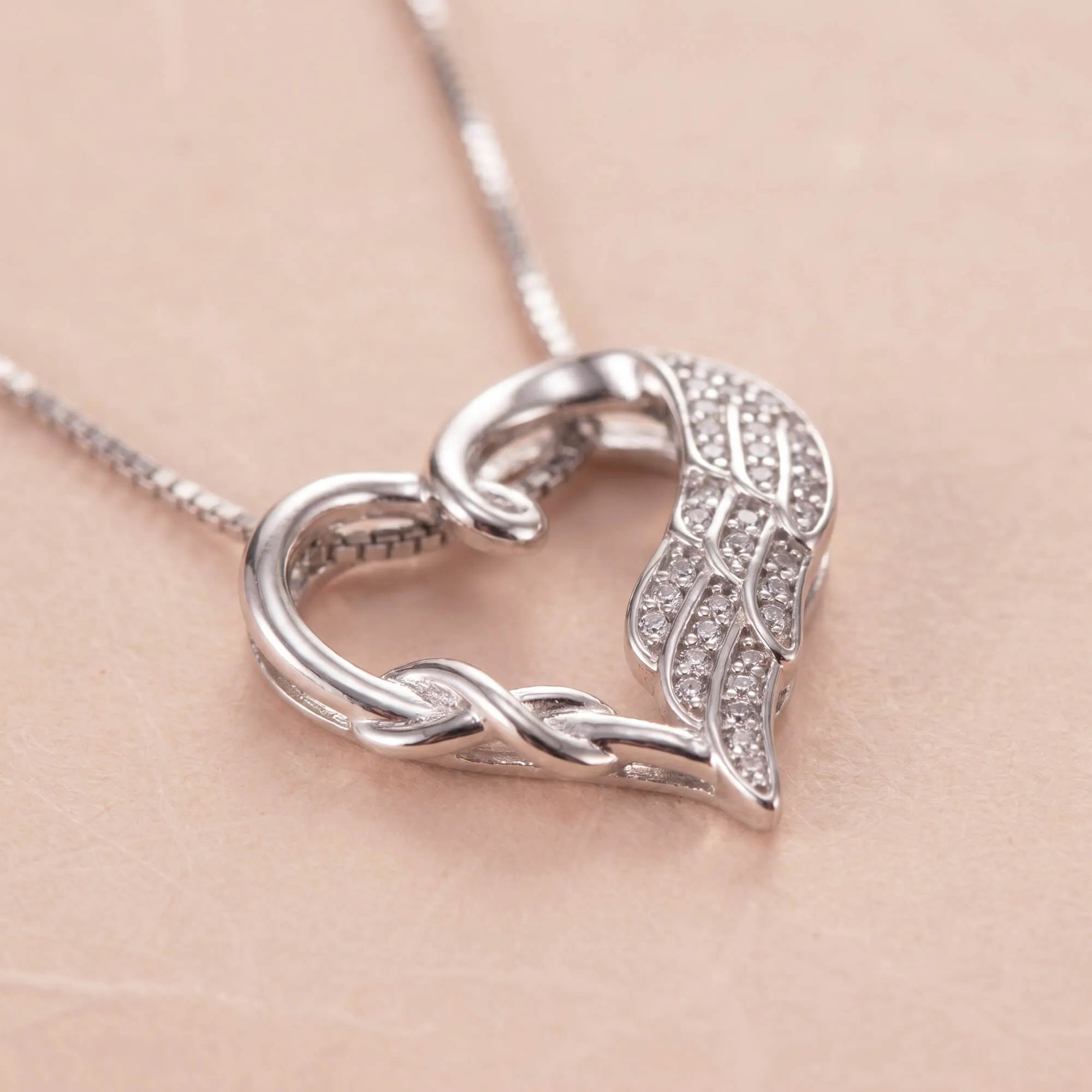 Close-up of silver heart necklace with angel wing and crystals