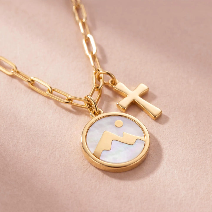 Close-up of gold necklace with mountain and cross charm
