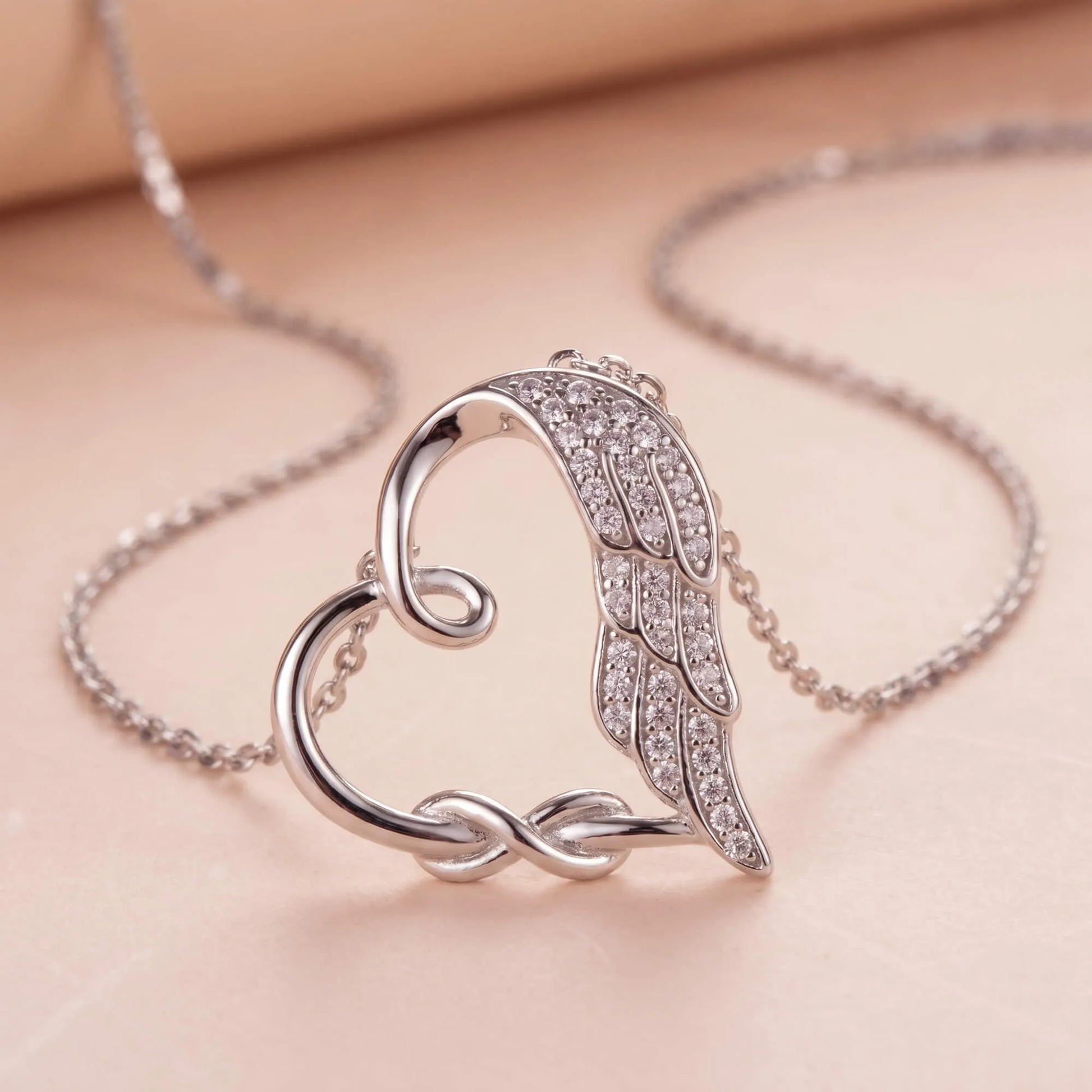 Close-up of silver heart necklace featuring infinity symbol and angel wing