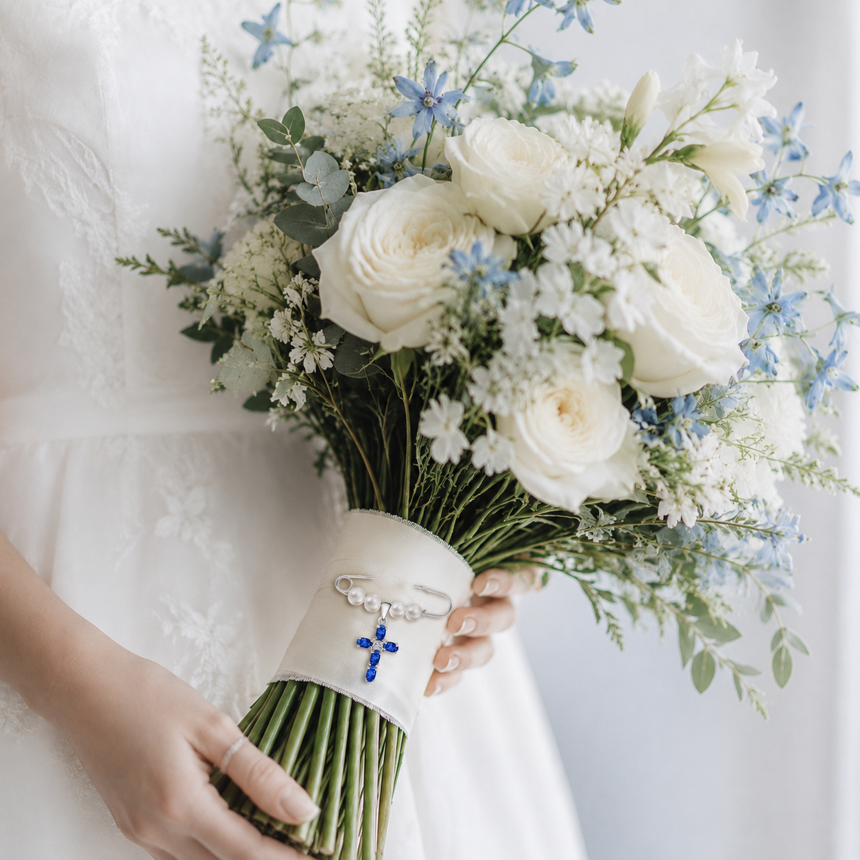 Something Blue Cross Pin attached to a bouquet with white roses and blue flowers