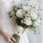 Something Blue Cross Pin attached to a bouquet with white roses and blue flowers