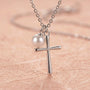 Close-up of silver cross necklace with pearl charm