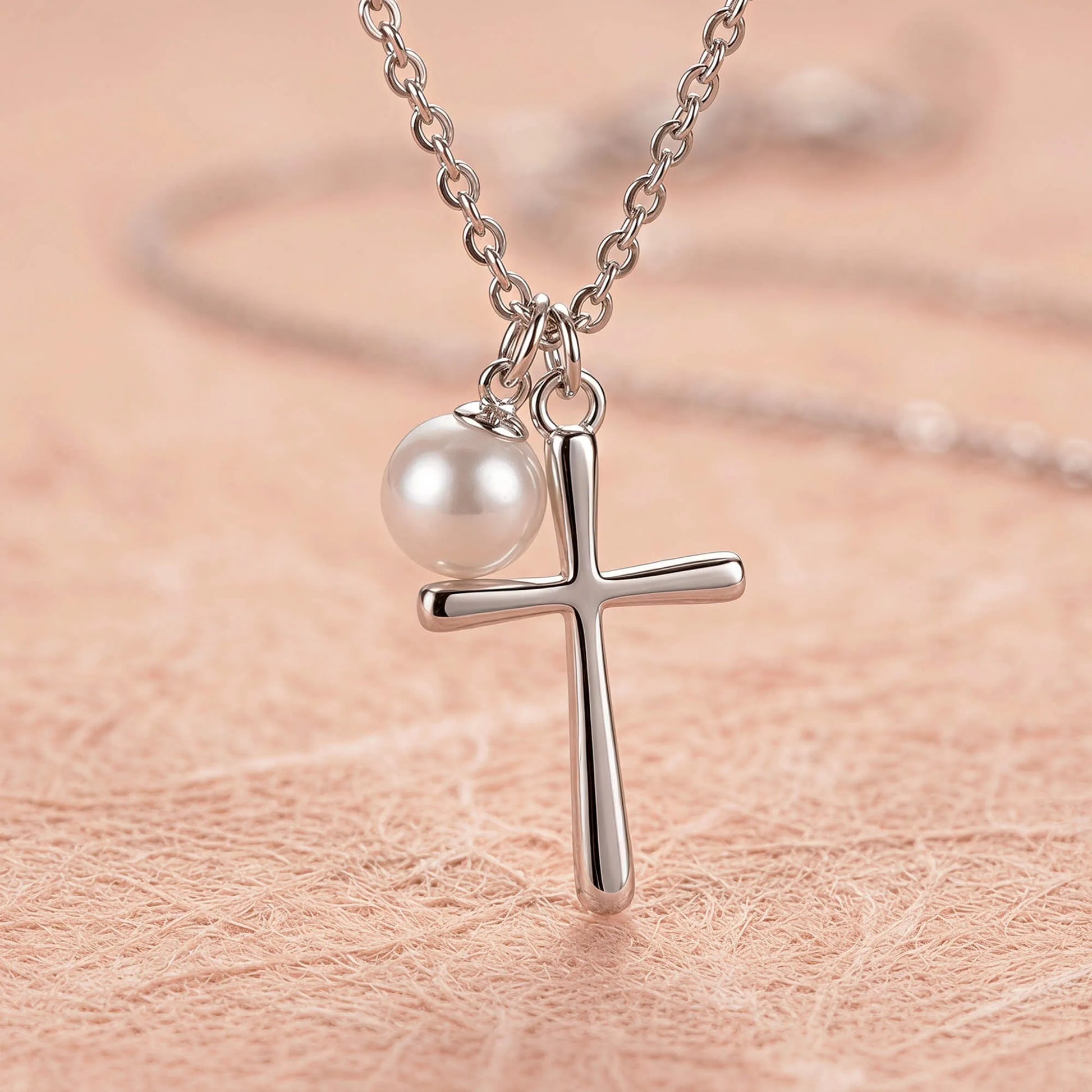 Close-up of silver cross necklace with pearl charm