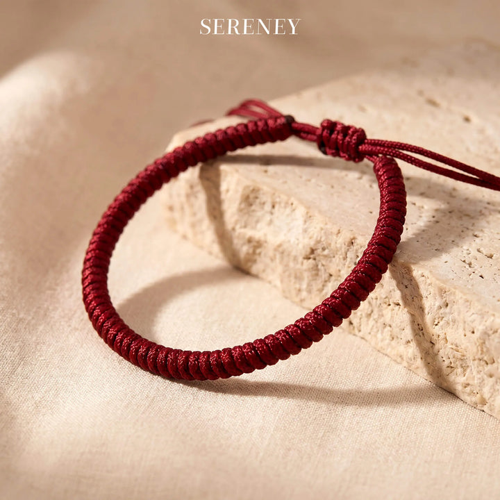 Red String Blessing Bracelet on a textured surface
