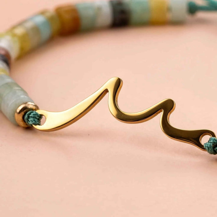 Gold wave charm detail on bracelet with braided cord and bead accents